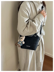 Detail view of black bucket bag with a cute teddy bear charm and sleek shoulder strap