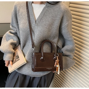 Detail of dark brown vintage handbag with leather texture and wooden bead charm