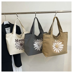 Close-up of canvas tote bag featuring floral daisy embroidery and reinforced shoulder handles