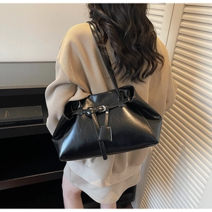 Detail of black matte tote bag with buckle strap and square tag charm on model