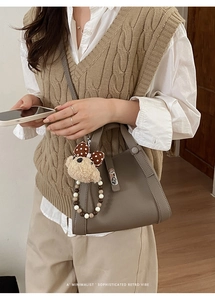 Chique taupe bucket bag met pluche beer hanger en kralenketting op een model