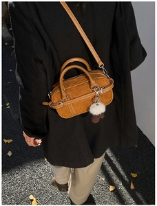 Close-up of camel brown suede crossbody bag with fluffy white pompom and shoulder strap