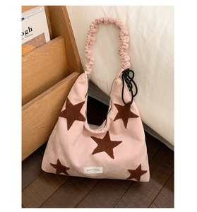 Pink velvet shoulder bag with brown star patches and pleated strap detail in cozy setting