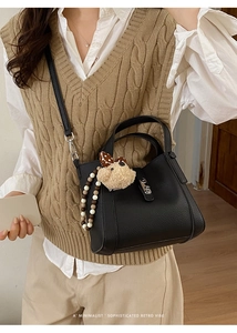 Detail van zwarte lederen emmer tas met zilveren sluiting en pluche hanger decoratie