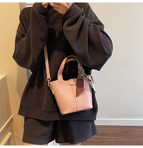 Detail view of light pink bucket bag featuring a decorative scarf and brand logo