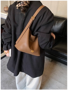 Sac seau en cuir marron avec logo doré porté par un mannequin dans un intérieur chic