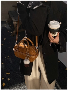 Brown suede crossbody bag with plush charms shown in an autumn street setting