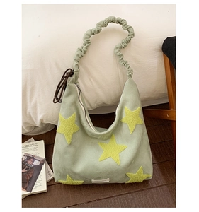 Detail of light green suede tote bag with yellow star patches and ruched strap design