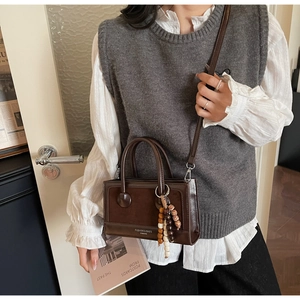 Detail of vintage brown leather crossbody bag with beaded pendant and gold strap buckle