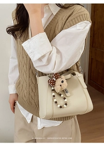 Detail van gebroken witte bucket bag met lychee-patroon, teddybeer hanger en slotje