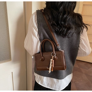 Detail of dark brown leather crossbody bag featuring a unique beaded tassel accessory