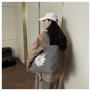 Détail du sac cabas en toile grise avec broderie de marguerite sur l'épaule