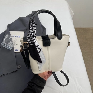 Detail of cream bucket bag with black handles and a houndstooth scarf on a grey suit jacket