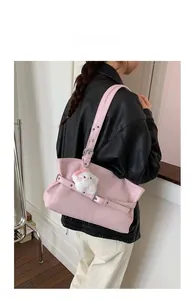 Detail view of the pink leather shoulder bag featuring metal buckles and a plush charm