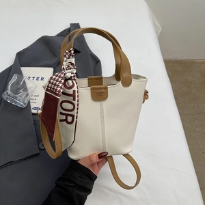 Detail of the elegant cream bucket bag featuring a brown handle and decorative silk scarf