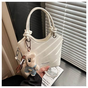 Detail of cream bucket bag with teddy bear charm and brand logo in soft window light