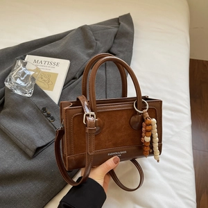 Close-up of brown patchwork handbag with wooden bead charm on a minimalist background