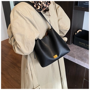 Détail du sac cabas en cuir grainé noir avec plaque dorée porté sur un trench-coat