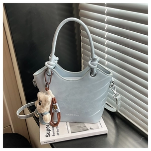 Detail of light blue textured bucket bag featuring decorative knots and cute teddy charm