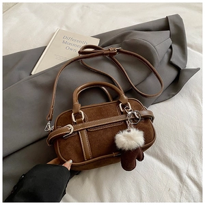 Close-up of brown suede crossbody bag featuring a plush white glove charm and dual handles