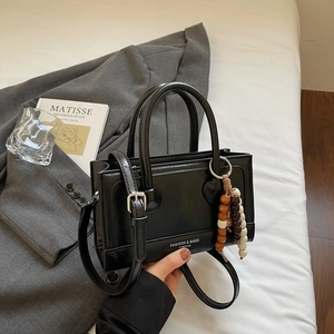 Chic black Boston handbag with wooden bead charm styled in a modern professional setting