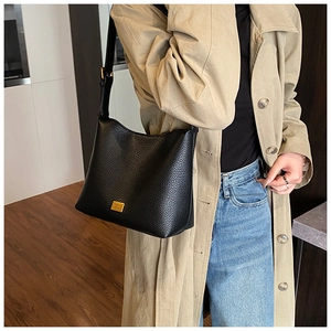 Détail du sac à bandoulière en cuir grainé noir avec plaque logo dorée et texture