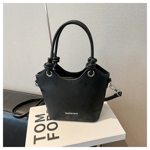 Detail view of black matte bucket bag with brand logo and silver hardware on a book