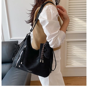 Detail of a large black tote bag with side silver zipper and long tassels on shoulder
