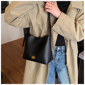 Détail d'un sac seau en cuir noir grainé avec logo doré porté à l'épaule pour femme