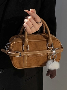 Brown suede Boston handbag with dual handles and plush charm in a minimalist style