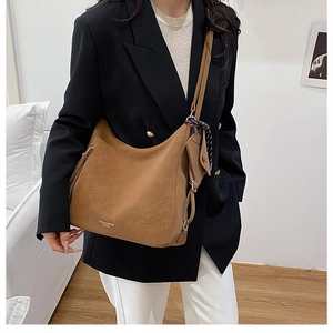 Detail of large brown suede hobo bag featuring branding and side zipper decoration