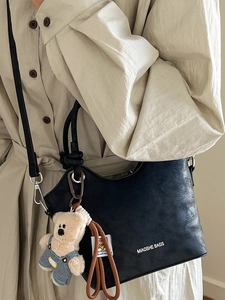 Minimalist black leather bucket bag with brand logo and cute plush bear charm