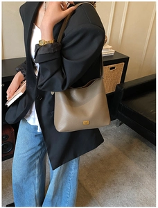 Détail du sac en cuir taupe avec plaque logo en métal doré et texture cuir grainé