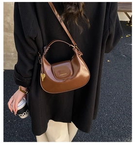 Detailed view of a brown glossy crescent bag with a gold heart pendant charm