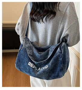 Detailed view of a large blue washed denim tote bag with white REPLACED logo lettering