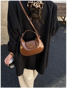 Detail view of brown glossy half-moon bag featuring a gold heart pendant and strap