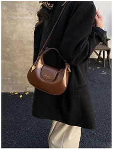 Brown patent leather crescent shoulder bag with heart charm shown in a street style shot
