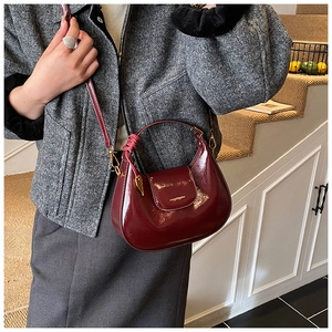 Detail of wine red glossy patent leather handbag with gold metal clasp and woven handle