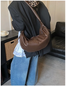 Detail of a dark brown pleated crescent bag worn as a shoulder bag in a lifestyle setting