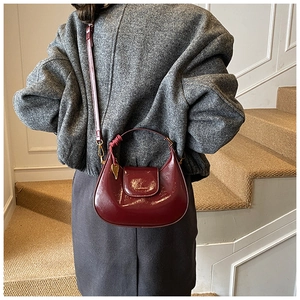 Detail of burgundy glossy leather handbag showing its crescent shape and gold logo finish