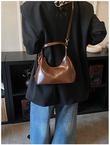 Détail d'un sac hobo en cuir verni marron foncé porté avec un blazer noir élégant
