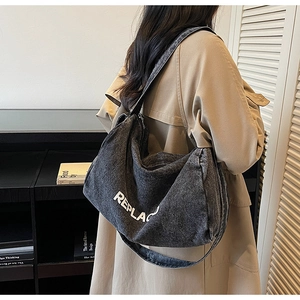 Close-up of black denim hobo bag featuring white REPLACE lettering and wide strap