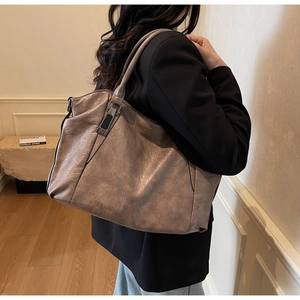 Side view of large vintage taupe leather tote bag worn by model in minimalist indoor setting