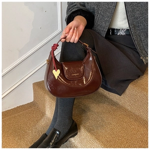 Close-up of a burgundy patent leather half-moon bag featuring a gold heart charm and tied knot