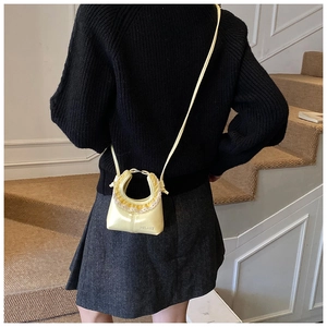 Detail of cream glossy leather mini bag with yellow lace trim and ring handle on model