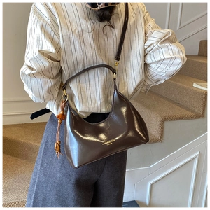 Détail d'un sac sous les aisselles en cuir brillant marron foncé avec logo doré et gland