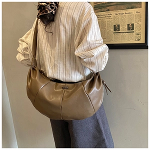 Detail of tan brown pleated shoulder bag with oval metal logo and wide strap