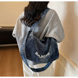 Detail of blue denim crossbody bag with white REPLACED embroidery and wide shoulder strap