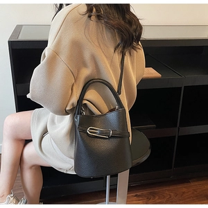 Detailed side view of black pebbled leather bucket bag with silver U-shaped buckle decoration