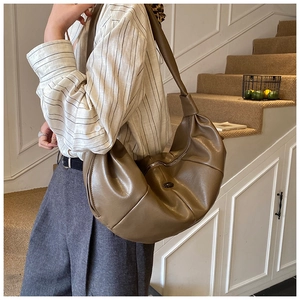 Detail view of large dark brown pleated leather hobo bag worn by a model on stairs